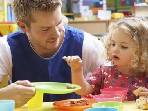 Man serving a child food in an early years setting, sitting at a table.