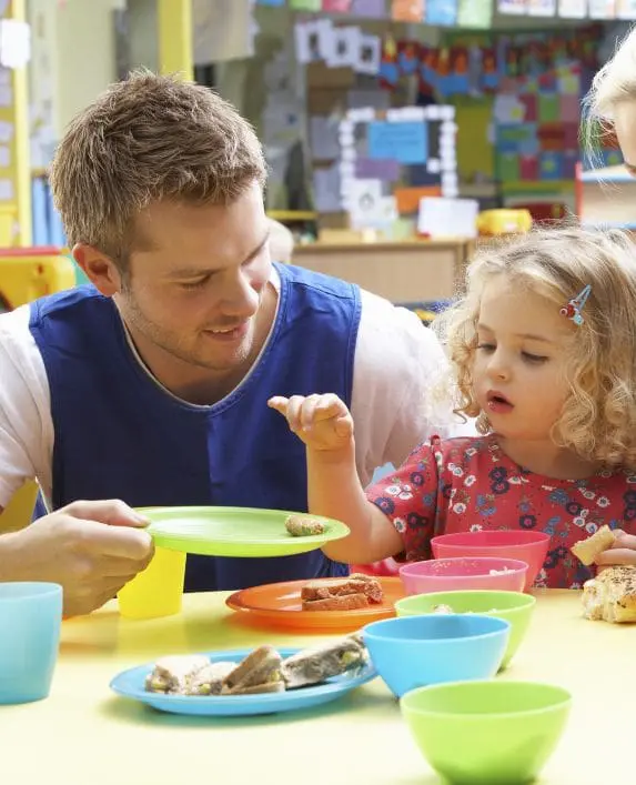 Man serving a child food in an early years setting, sitting at a table.