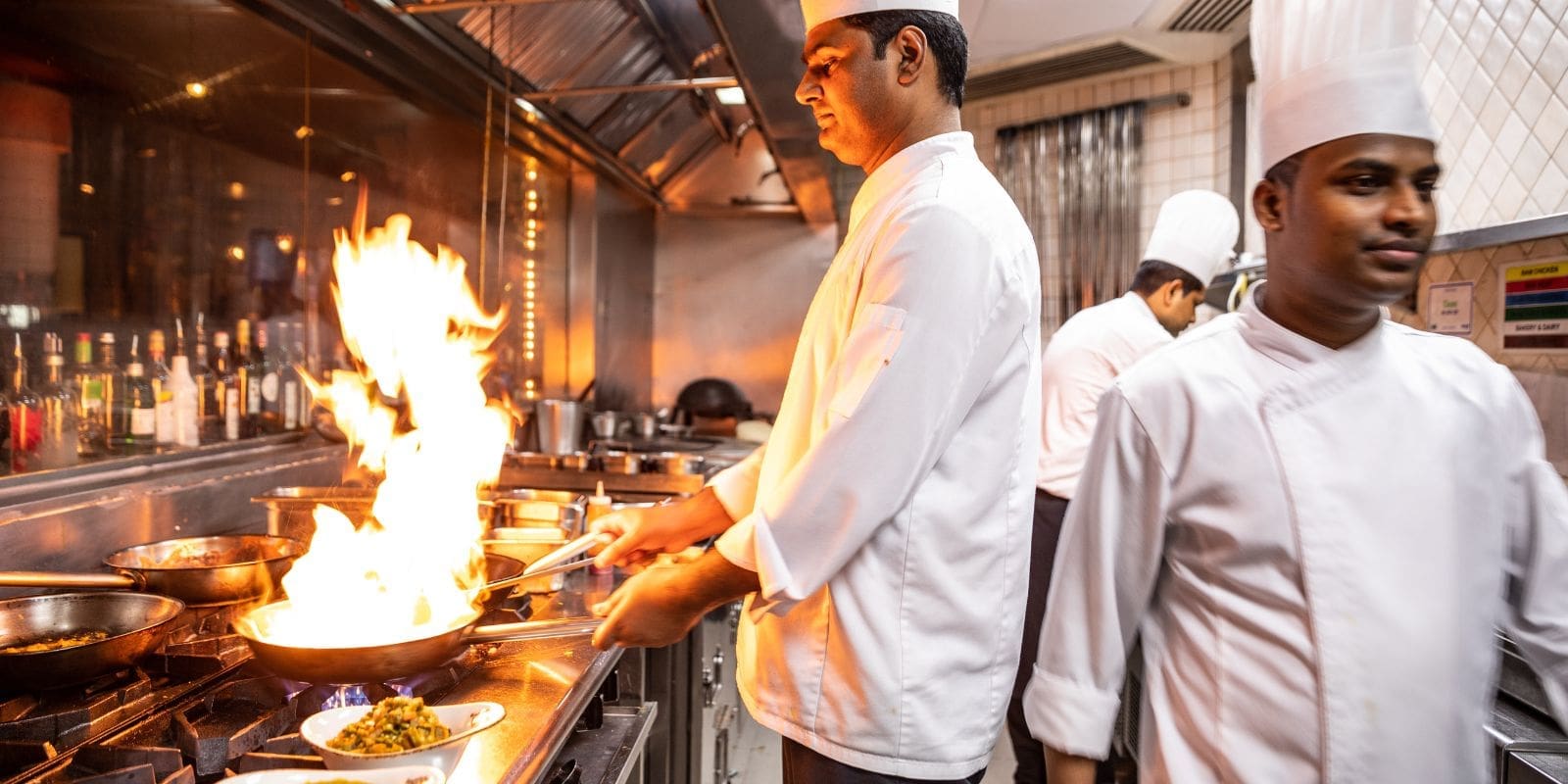 Chef cooking with a frying pan with a large flame in a restaurant setting