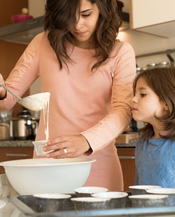 Childminder with a child making some cakes in a home kitchen.