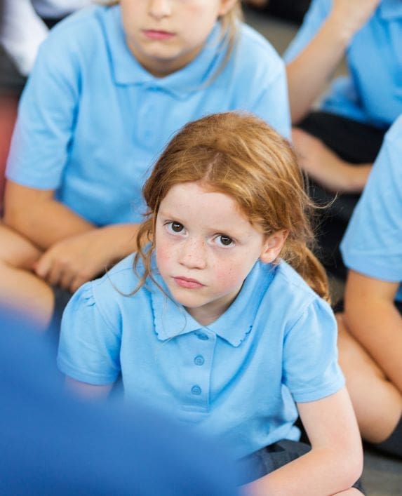 Girl in a school classroom looking serious looking straight at the camera.