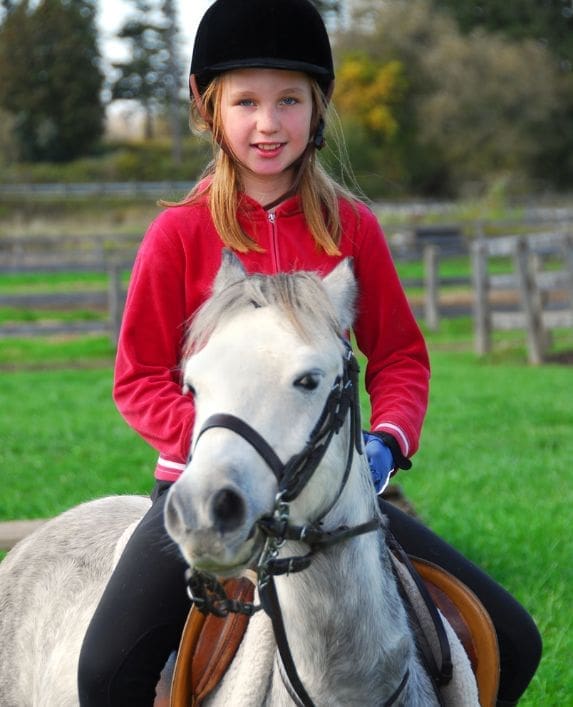 A girl on a white horse with a helmet on her head about to go riding.