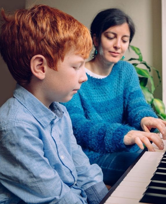 Lady piano teacher teaching a boy to play piano.