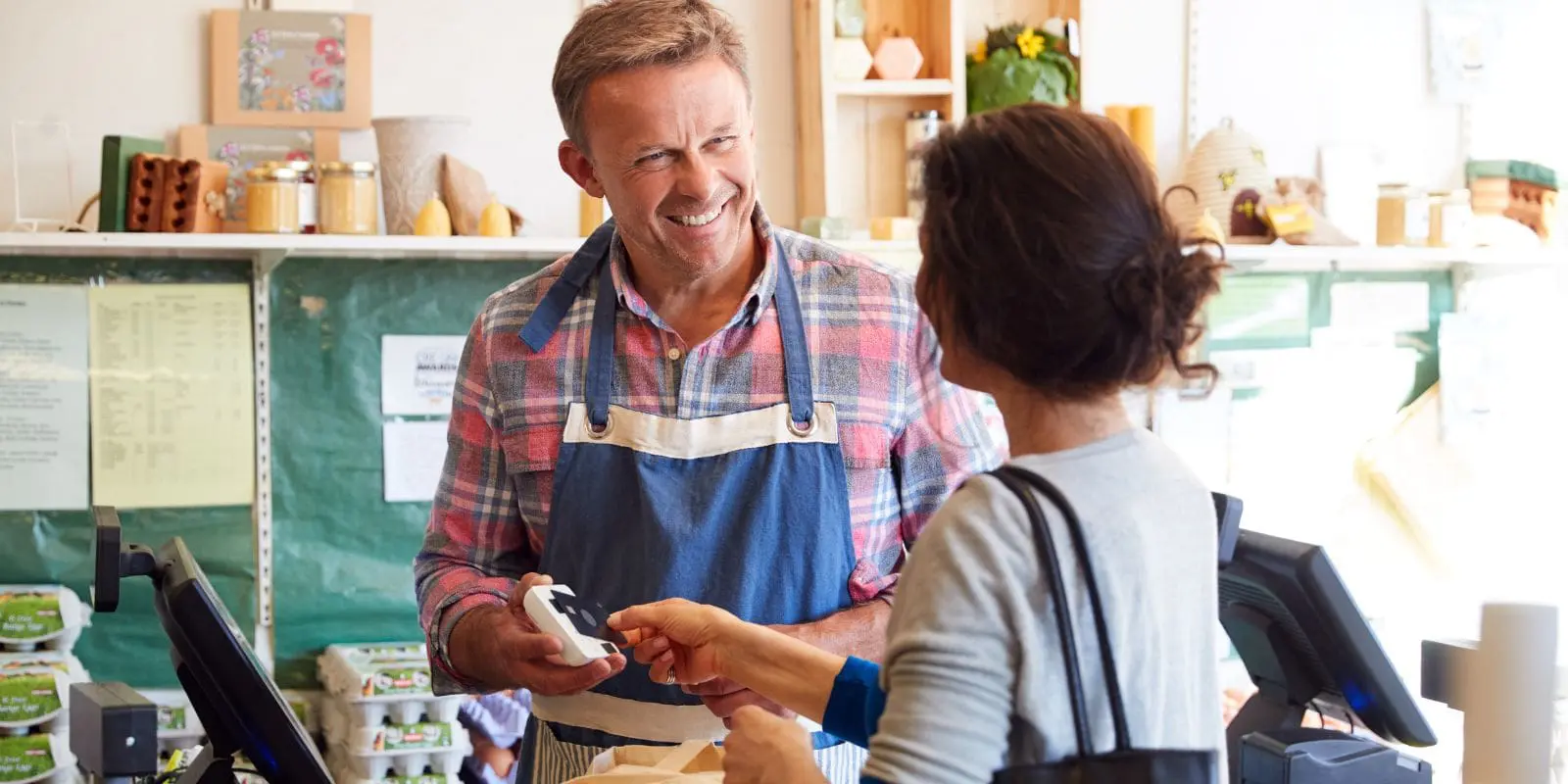 A man in a farm shop serving a lady who has a bag of food.