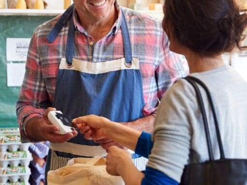 Man in an apron serving a lady in a farm shop.