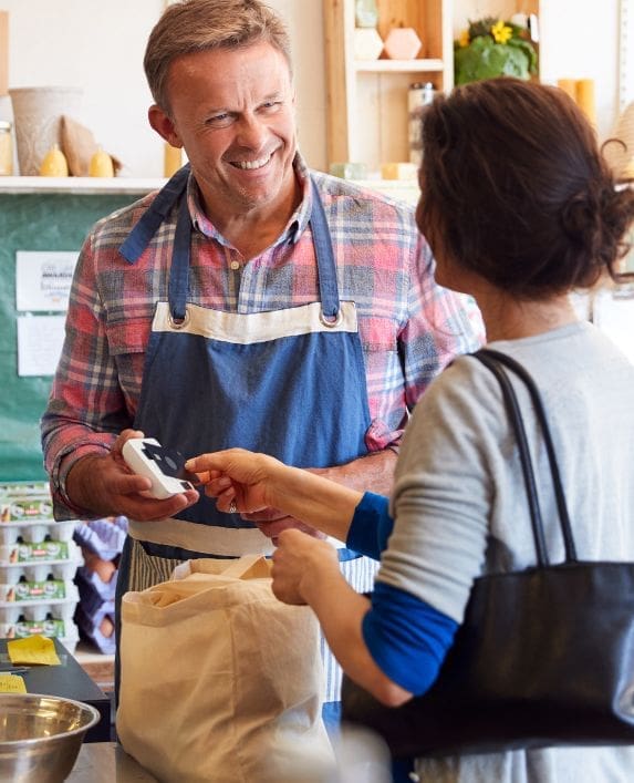 Man in an apron serving a lady in a farm shop.