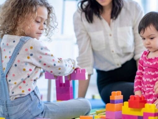 Nanny with two children playing with lego on a play mat