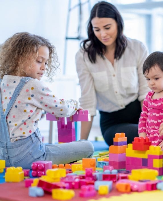 Nanny with two children playing with lego on a play mat