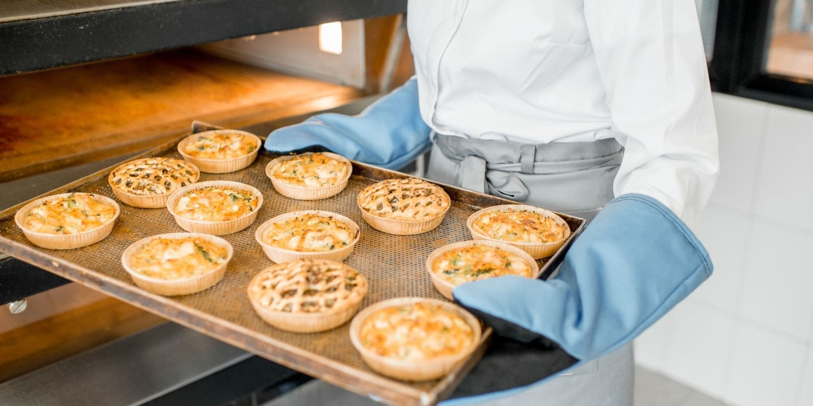 Person holding a tray of pies in a bakery processing plant.