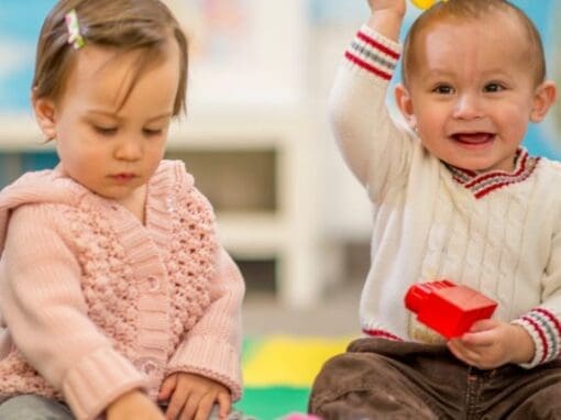 Two babies playing on a rug with toys