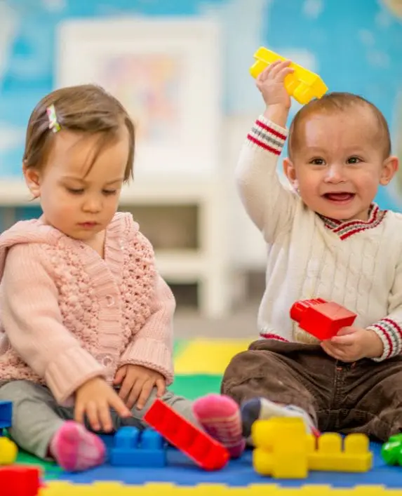 Two babies playing on a rug with toys