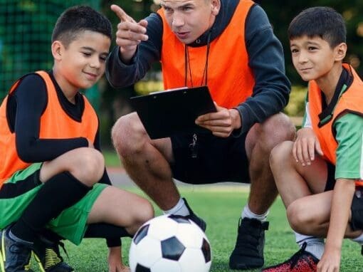 Two boys with their football coach, who is pointing at something.