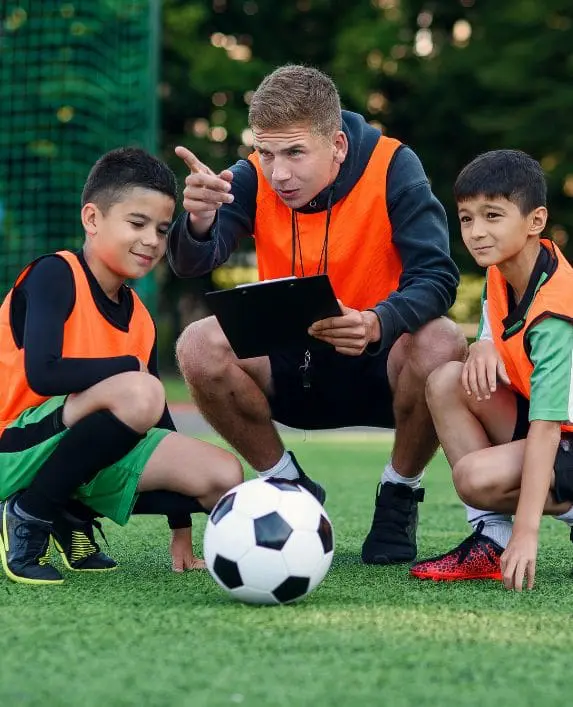 Two boys with their football coach, who is pointing at something.