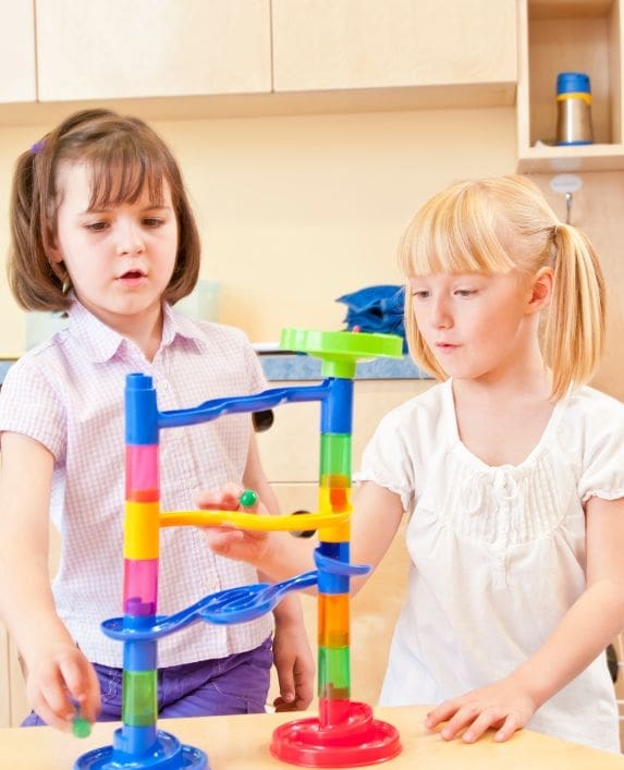 Two children playing with a marble run at nursery.