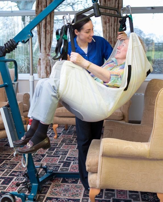 A lady being moved in a sling hoist by her carer.