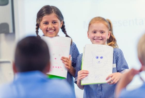 Two school girls side by side showing a teacher a painting.