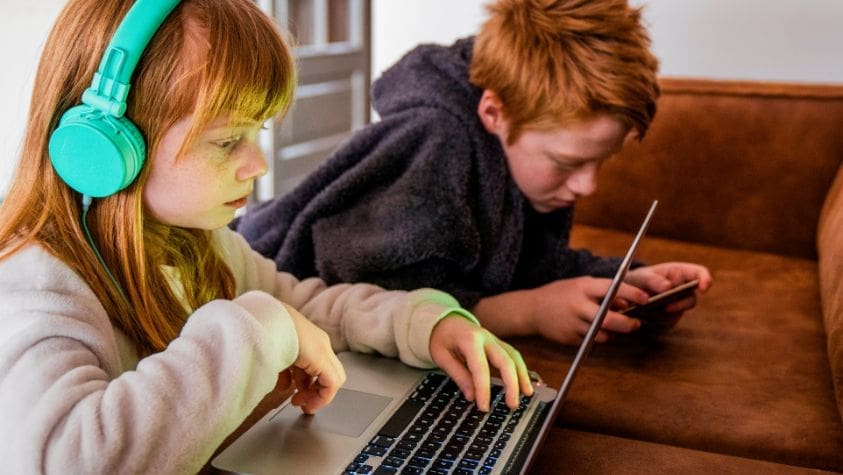 Two children looking at laptops and electronic devices